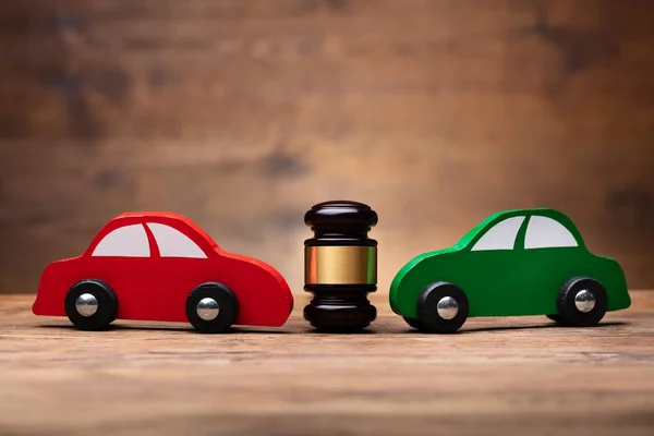 Wooden Mallet Between Two Red And Green Car On Wooden Surface