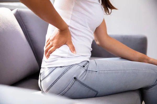 Frau Sitzt Auf Sofa Und Leidet Unter Rückenschmerzen — Stockfoto