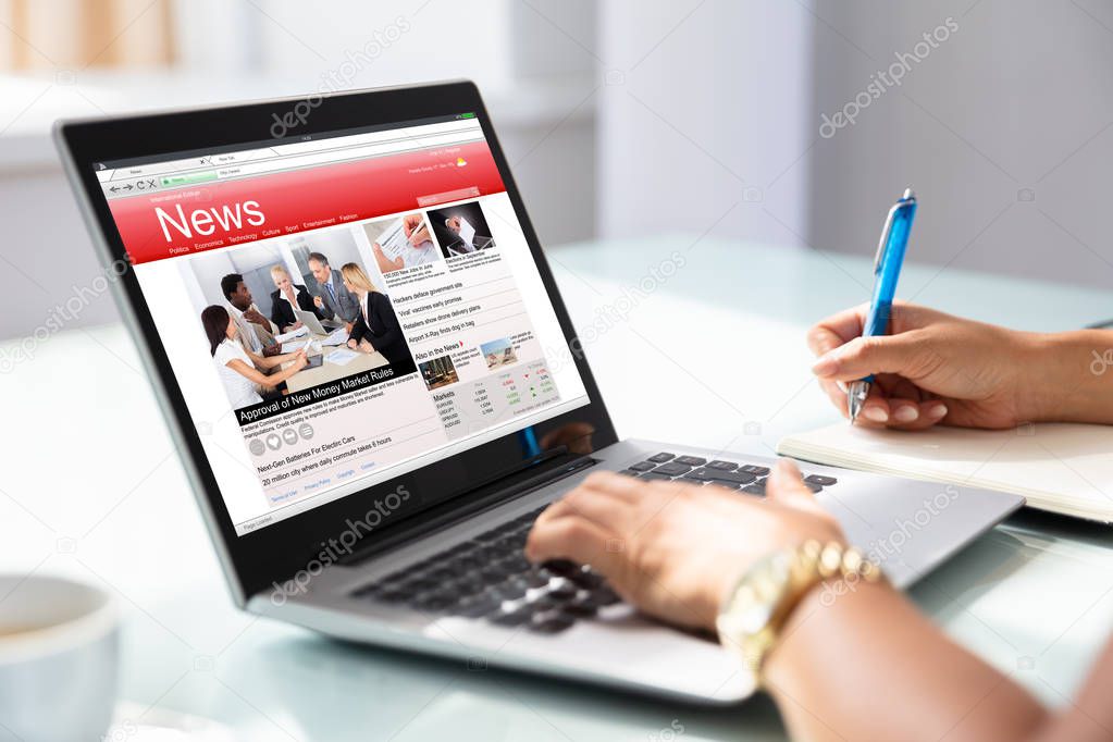 Close-up Of Businesswoman's Hand Checking Online News On Laptop In Office