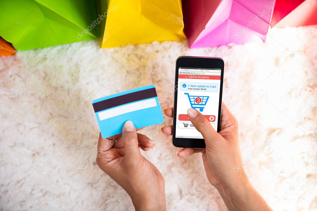 Elevated View Of Woman's Hand Shopping Online On Mobile Phone Over Carpet