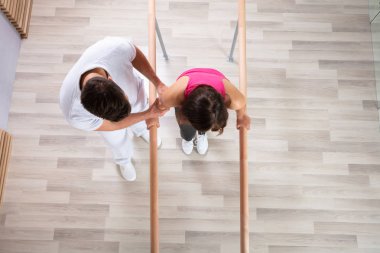 Bayan hasta fiziksel terapist tarafından Küpeşte desteği ile yürürken yardımcı