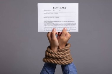 Woman's Hand Tied With Rope Holding Contract Form On Grey Background clipart