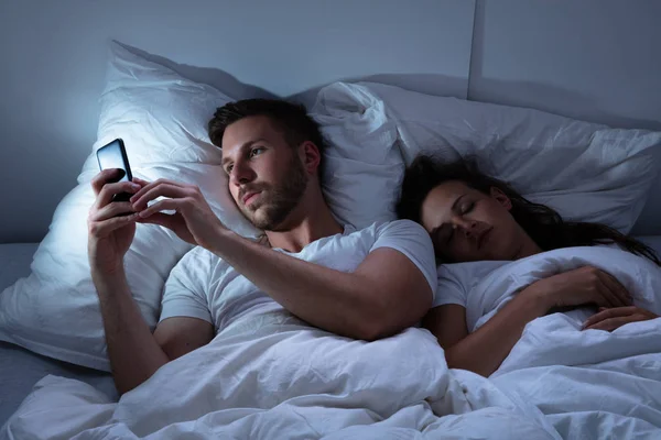 Jovem Usando Celular Enquanto Sua Esposa Senta Cama Noite — Fotografia de Stock