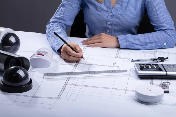 Architect Drawing Blueprint With Various Security Equipment On Desk