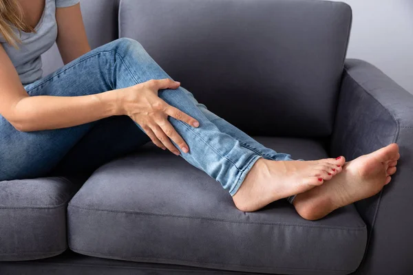 負傷した右足を見てソファの上に座っている女性 — ストック写真