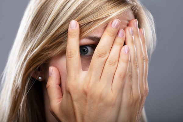 Close-up Of A Scared Woman Peeking Through Fingers