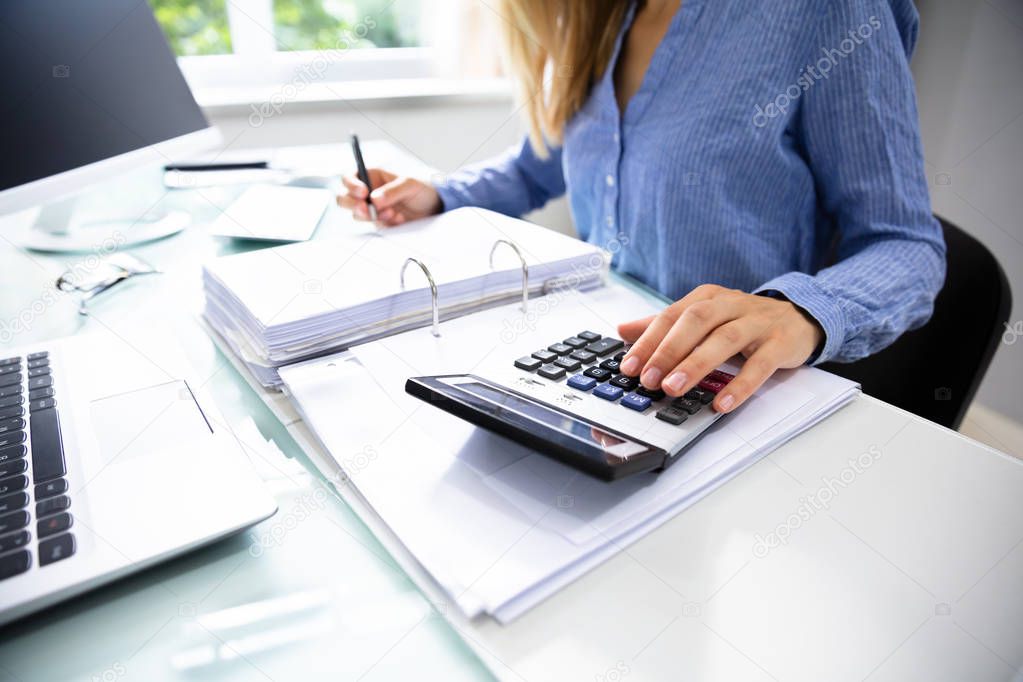 Close-up Of A Businesswoman's Hand Calculating Invoice Over Desk In Office
