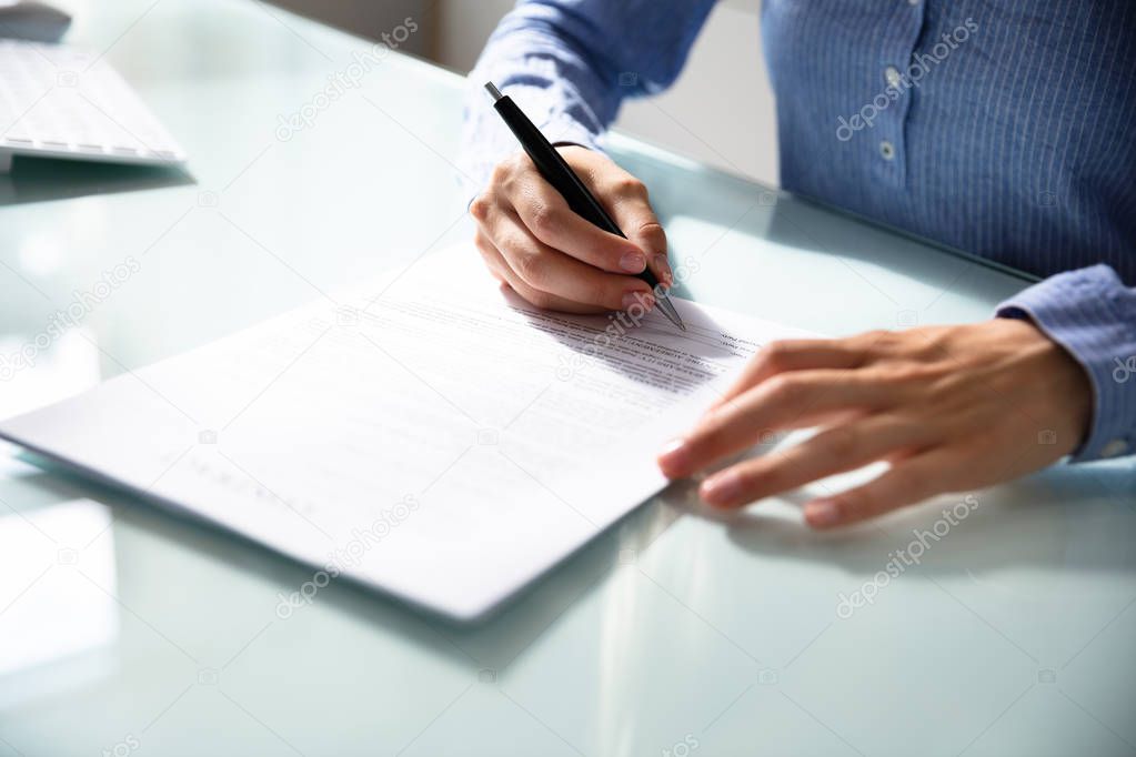 Businesswoman's Hand Signing Contract With Pen Over Desk