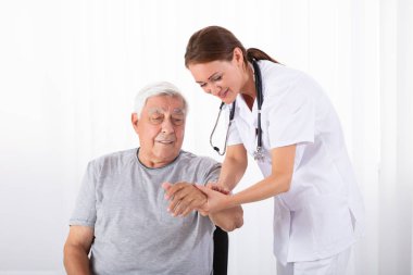 Genç erkek doktor klinik kıdemli erkek hastanın darbe incelenmesi