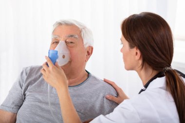 Genç erkek doktor Holding oksijen maskesi kıdemli erkek hastanın yüzüne