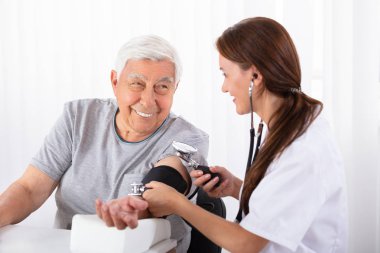 Young Female Doctor Checking Blood Pressure Of Senior Male Patient In Clinic clipart