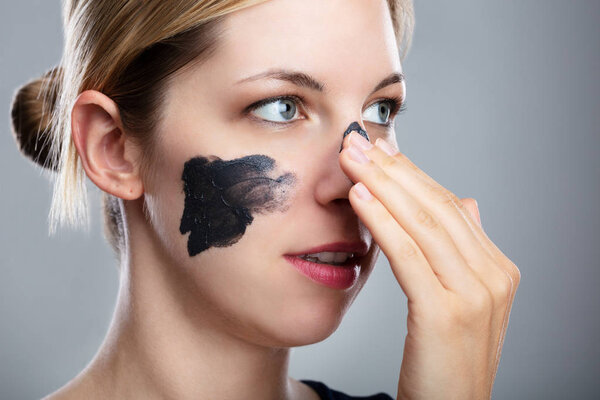 Portrait Of A Smiling Young Woman Applying Activated Charcoal Mask On Her Face