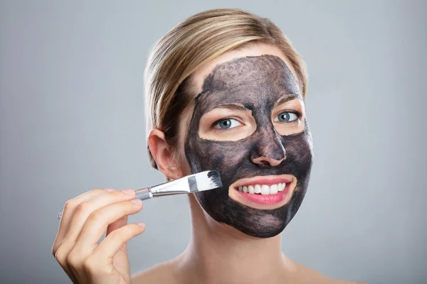 Ung Kvinna Applicera Aktivt Kol Ansiktsmask Med Borste Grå Bakgrund — Stockfoto