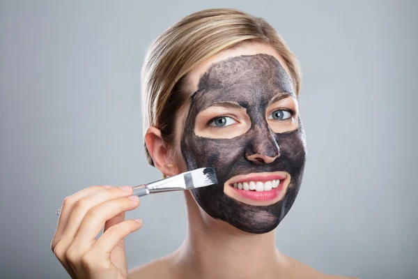 Mujer Joven Aplicando Mascarilla Carbón Activado Con Cepillo Sobre Fondo —  Fotos de Stock