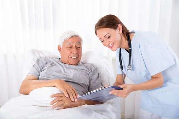 Jonge Vrouwelijke Verpleegkundige Met Klembord Senior Mannelijke Patiënt Bezoeken — Stockfoto