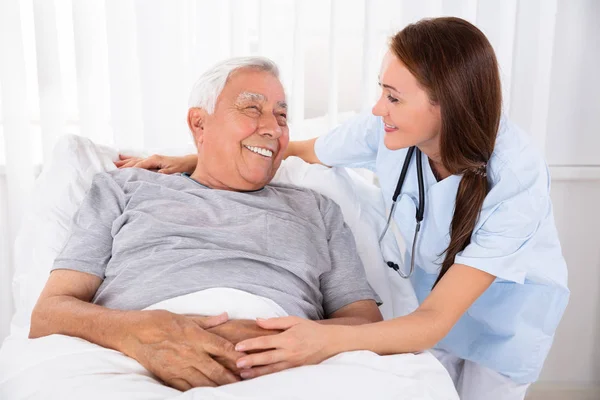 护士看着快乐的男性病人躺在床上的诊所 — 图库照片