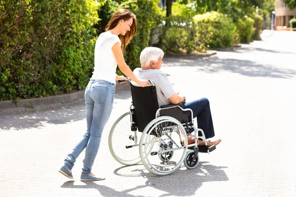 Młoda Kobieta Pomagając Ojcu Niepełnosprawnych Wózku Inwalidzkim Zewnątrz — Zdjęcie stockowe