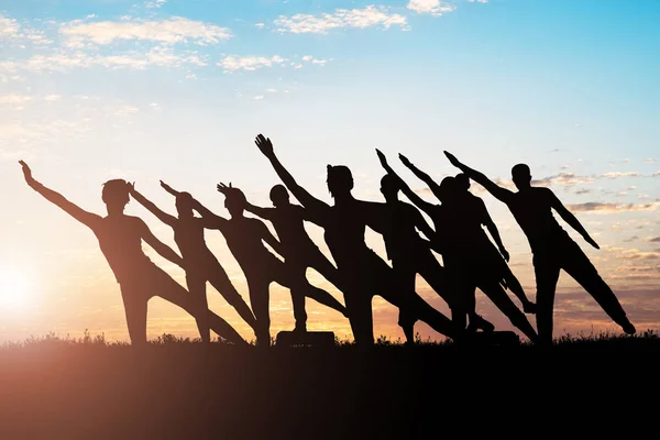 Silueta Personas Haciendo Ejercicio Estiramiento Contra Cielo Atardecer —  Fotos de Stock