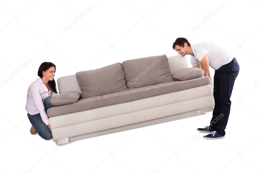 Young Couple Lifting Sofa On White Background