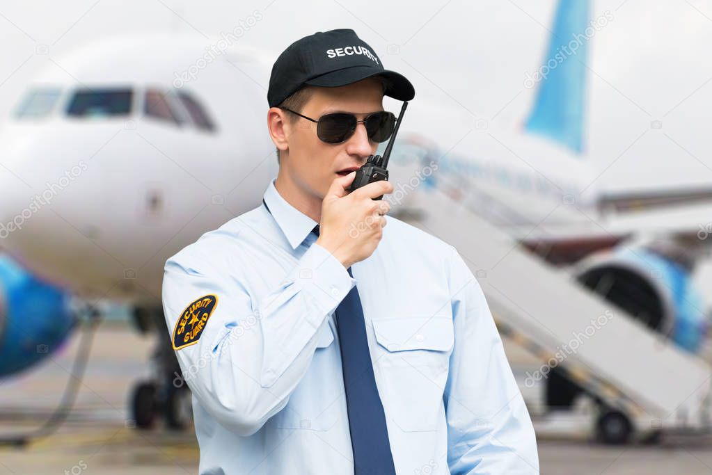 Portrait Of A Male Security Guard Talking On Walkie Talkie At An Airport
