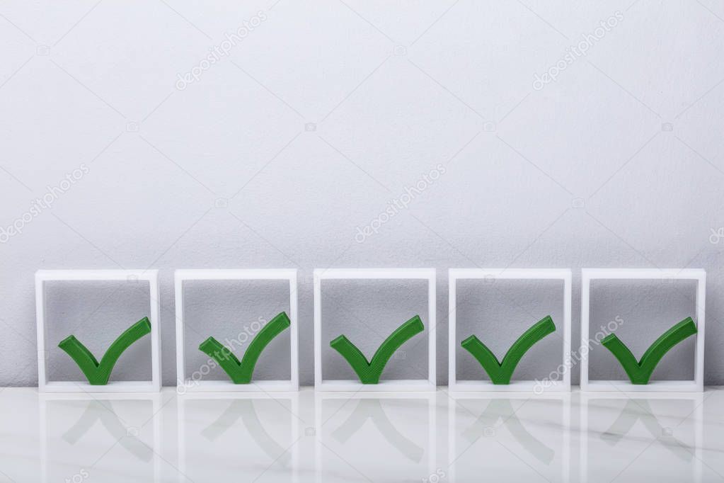 Row Of Green Check Marks In Boxes On Reflective Desk
