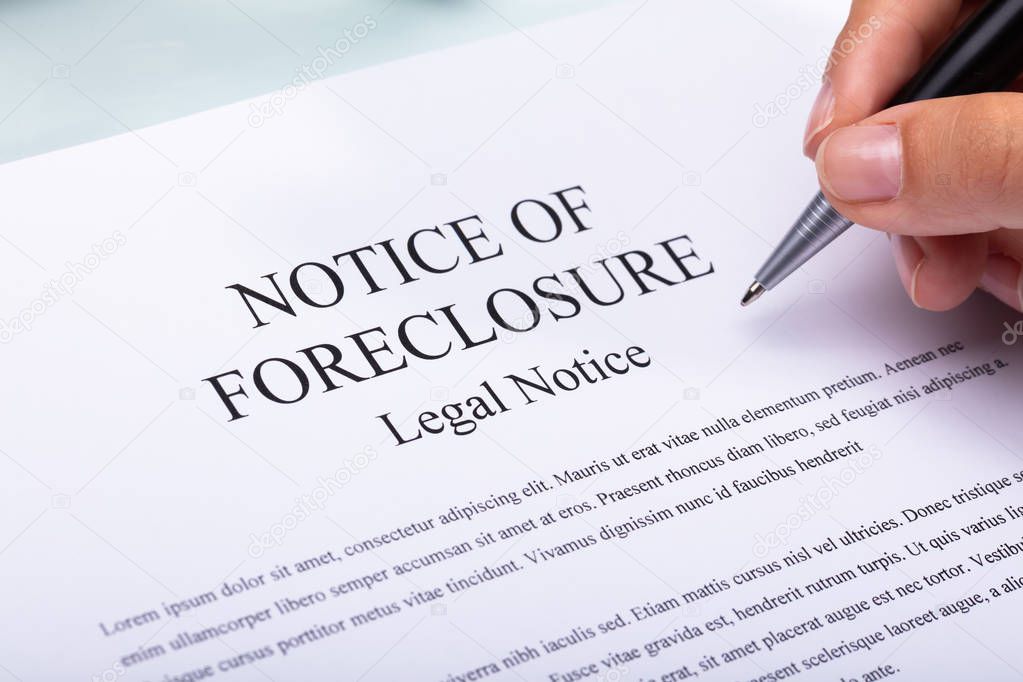 Close-up Of A Woman's Hand Holding Pen Over Notice Of Foreclosure Document