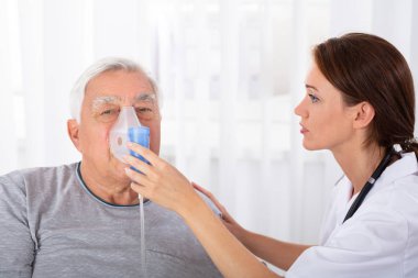Genç erkek doktor Holding oksijen maskesi kıdemli erkek hastanın yüzüne