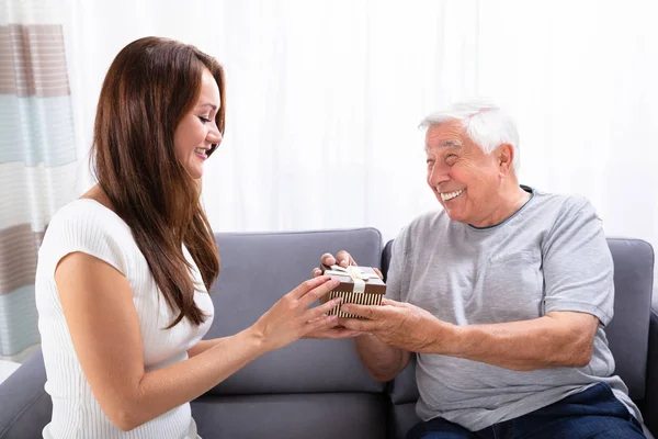 Woman Giving Gift Her Happy Father Sitting Sofa — Stock Photo, Image