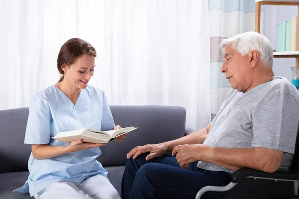 Verpleegkundige Leesboek Voor Gehandicapte Senior Man Zittend Rolstoel — Stockfoto