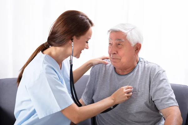 Leende Ung Sjuksköterska Undersöker Senior Mannen Med Stetoskop Hemma — Stockfoto
