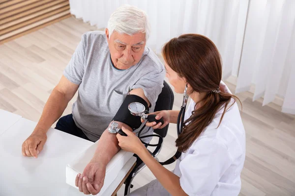Jonge Vrouwelijke Arts Controleren Bloeddruk Van Senior Mannelijke Patiënt Kliniek — Stockfoto
