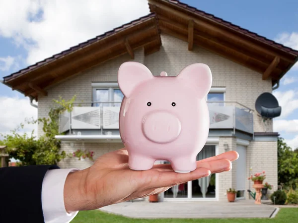 Affärsmans Handen Håller Piggybank Framför Huset — Stockfoto