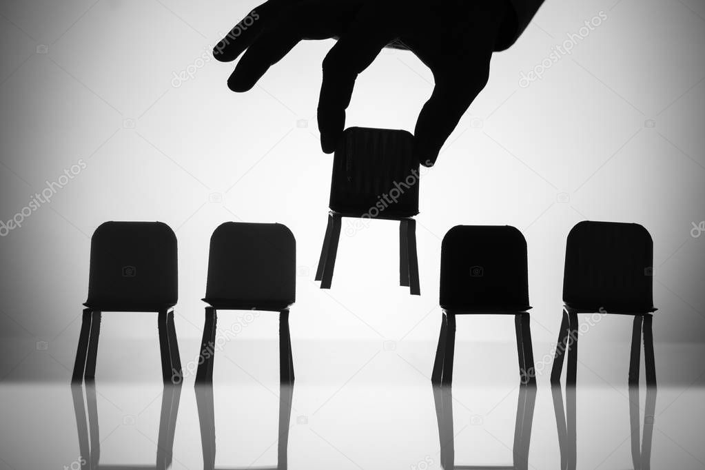 Close-up Of A Businessperson's Hand Picking Up Chair Amongst Other In A Row