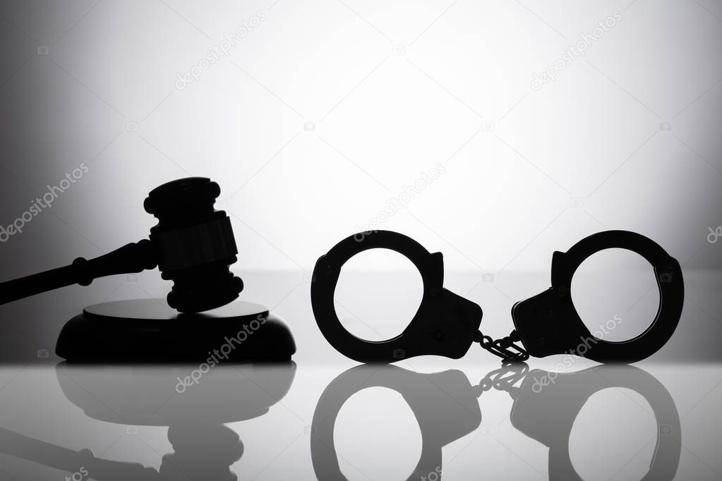 Silhouette Of Handcuff Near Gavel With Sounding Block On Reflective Background