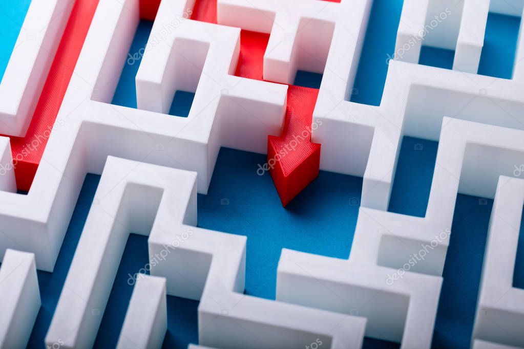 Elevated View Of Red Arrow At The Center Of White Maze On Blue Surface