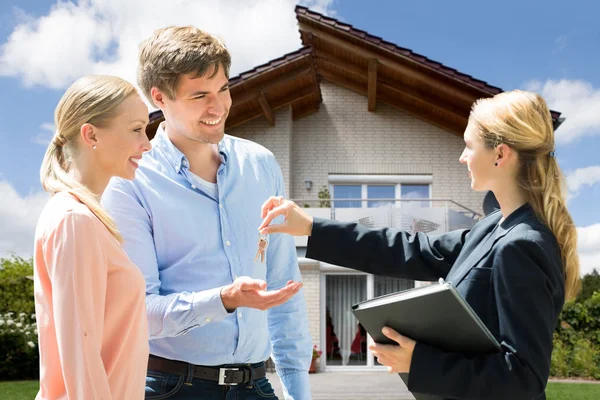 Lächelnde Immobilienmaklerin Übergibt Schlüssel Für Neues Haus Junges Paar — Stockfoto