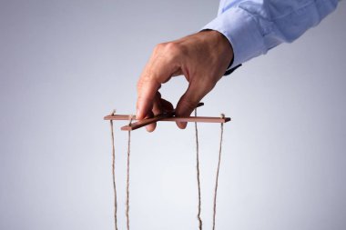 Close-up Of A Person's Hand Manipulating Marionette With String On Gray Background clipart
