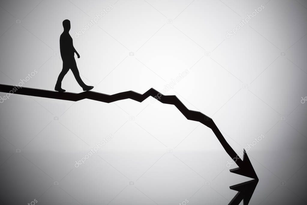 Silhouette Of A Person Walking On Arrow Moving In Downward Direction On Reflective Desk