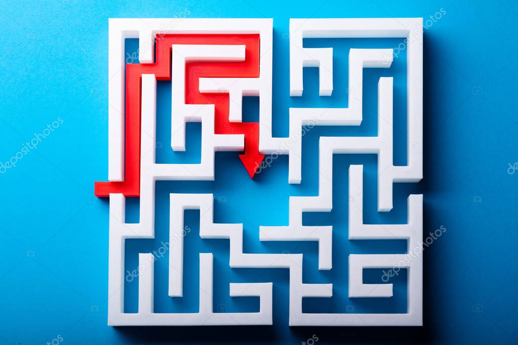 Elevated View Of Red Arrow At The Center Of White Maze On Blue Surface