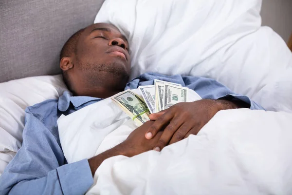 紙幣の束が付いているベッドで寝ているアフリカ人の人 — ストック写真