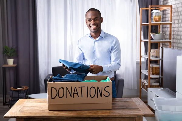 Happy African Man Putting Clothes In Donation Box