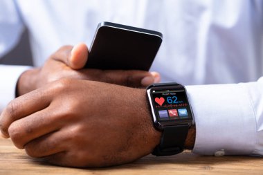 Hareket eden telefon ile kalp hızı gösterilen Smartwatch tutan bir erkek eli Close-up