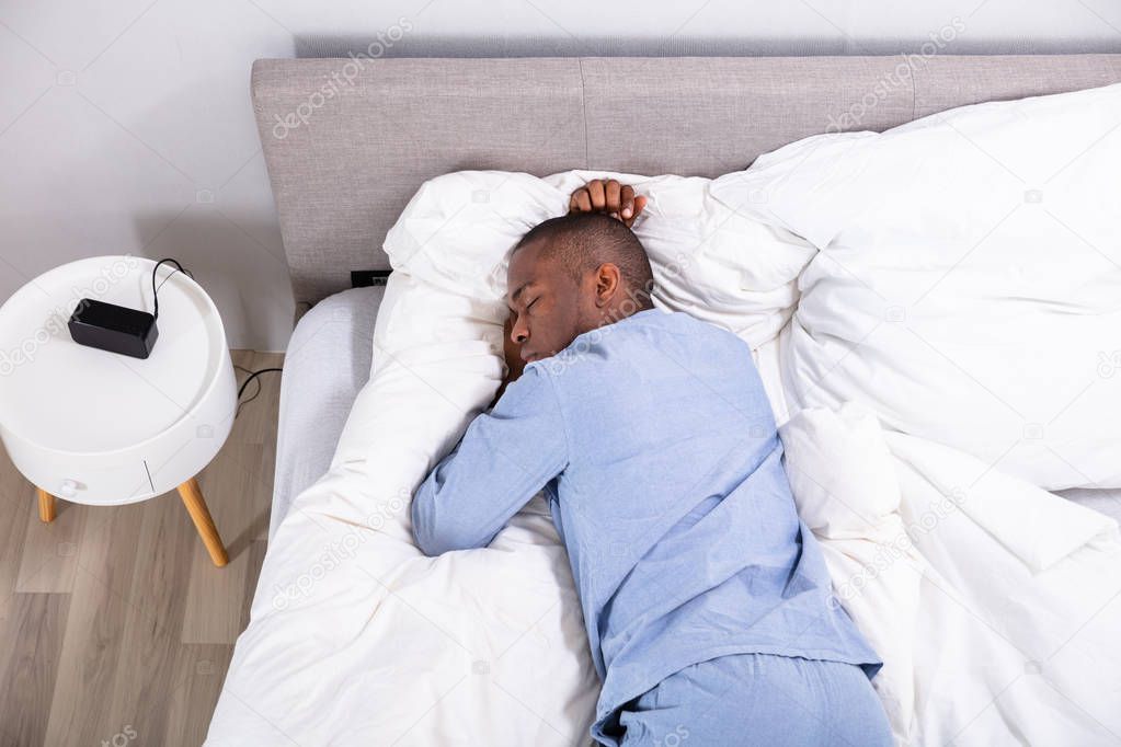 High Angle View Of Young African Man Sleeping On Bed In Bedroom