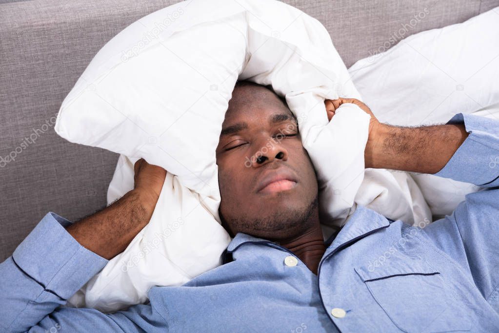 Man Covering His Ears With Pillow While Lying On Bed