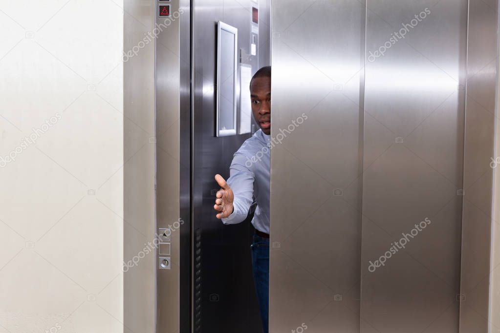 Young African Man Trying To Stop Elevator Door With His Hand