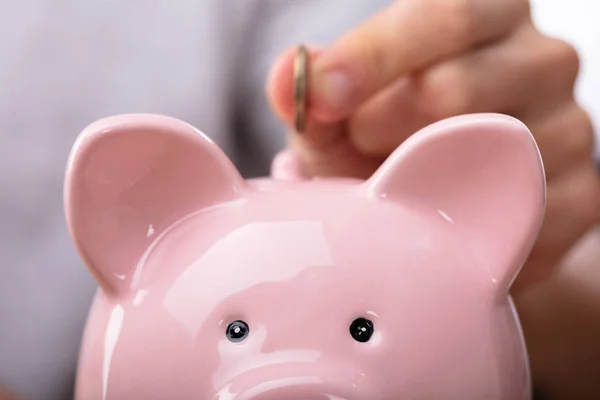 ピンクの貯金箱にコインを入れる人の手のクローズアップ — ストック写真