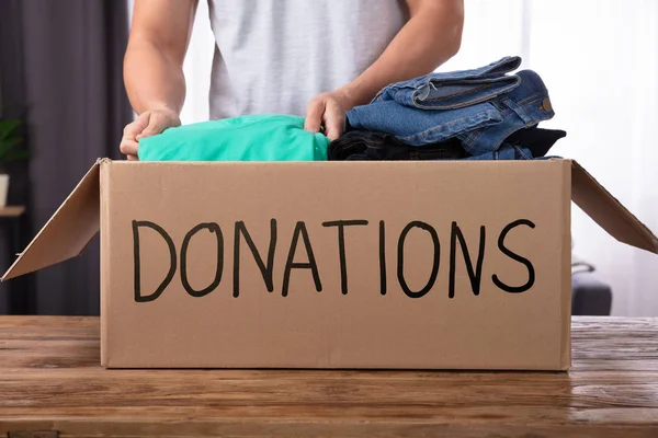 Young Man Donating Clothes Donation Box Wooden Desk — Stock Photo, Image