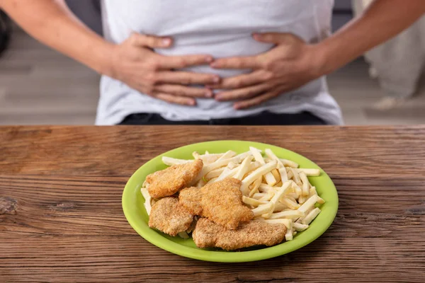 胃の痛みを持つ人の前でプレート上の不健康な食品 — ストック写真