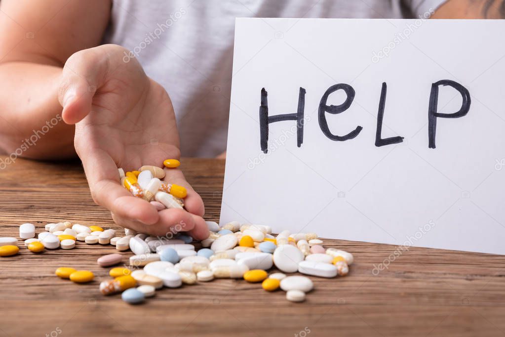 Man's Hand Holding Pills With Help Text On Paper Over Wooden Desk