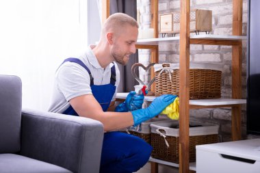 Erkek kapıcı üniformalı ahşap raf silerek gülümseyen